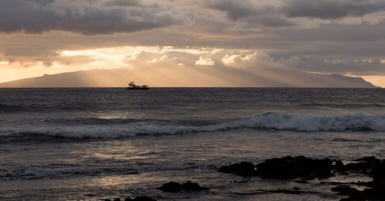 Um barco solitário navega no oceano ao pôr do sol