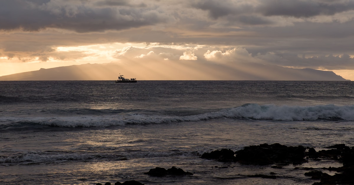 Um barco solitário navega no oceano ao pôr do sol