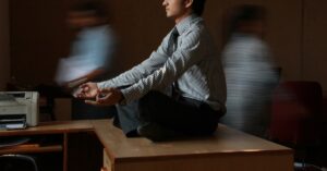 homem com camisa social listrada branca e azul sentado em mesa de madeira marrom