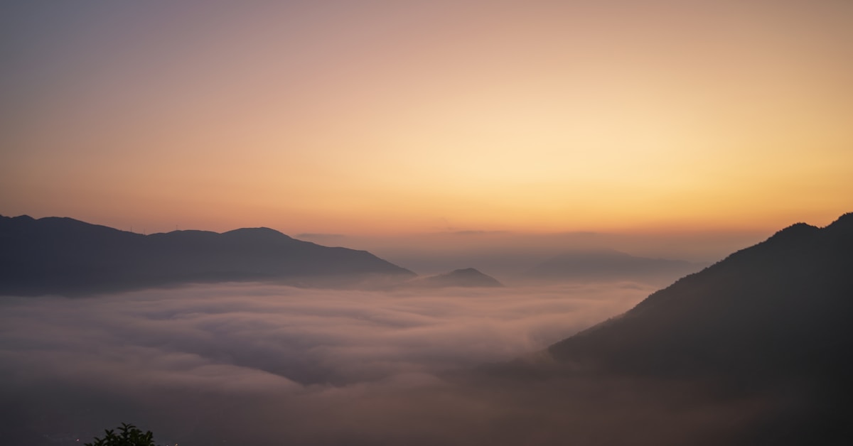 Vale montanhoso enevoado ao amanhecer com céu levemente alaranjado