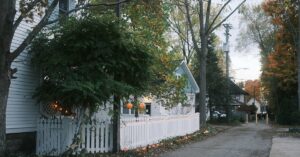 Uma cerca branca de estacas margeia uma rua arborizada no outono