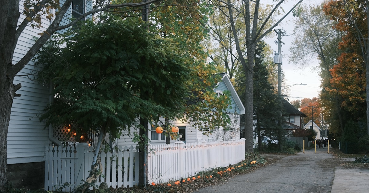 Uma cerca branca de estacas margeia uma rua arborizada no outono
