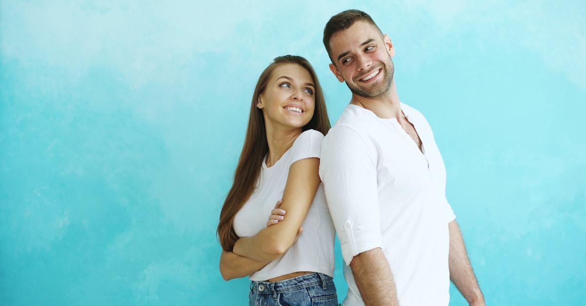 Casal sorrindo de costas um para o outro contra a parede azul